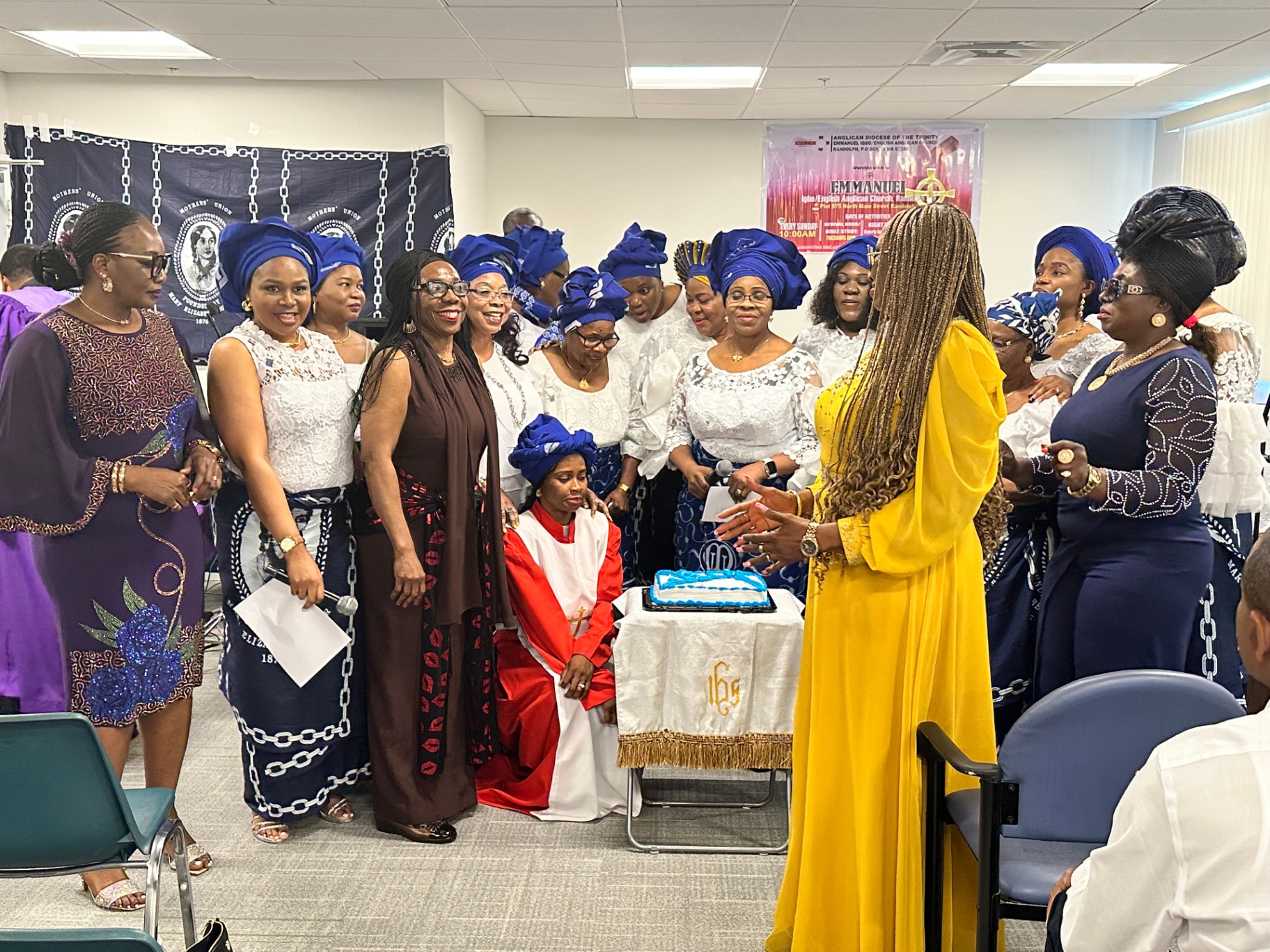 Women of Emmanuel gathered around the Mother's Sunday cake in blue gele head wraps